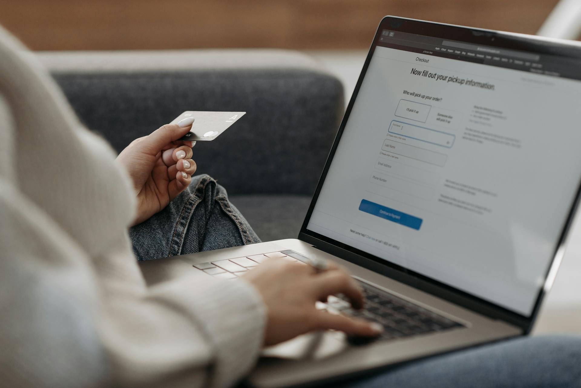 A woman typing on a computer, holding a credit card in her other hand.
